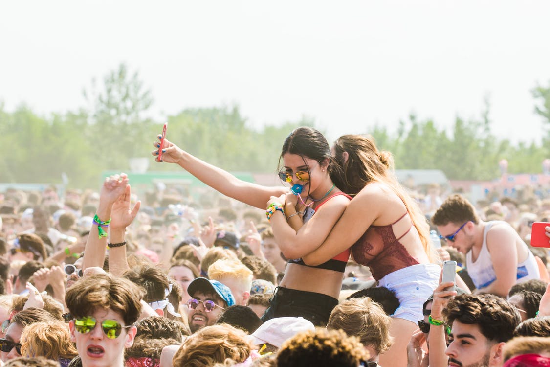 Friends taking a selfie on shoulders in a sunny festival crowd
