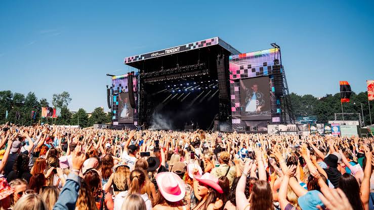 Packed daytime festival crowd in front of a large outdoor stage