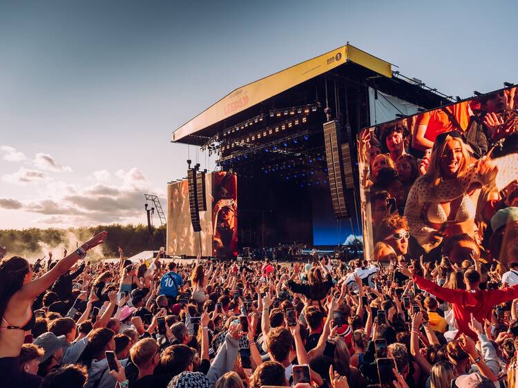 Festival crowd with hands up in front of a main stage at sunset