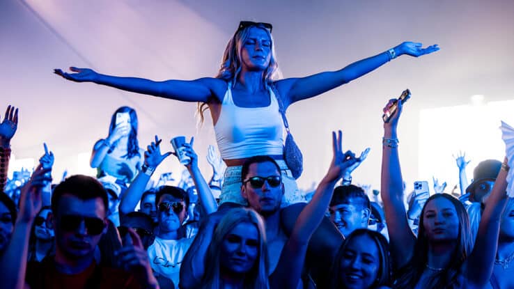Festival-goer on shoulders with arms outstretched under blue stage lights